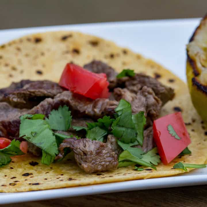 Steak tacos on a tortilla with fresh cilantro and tomatoes, served with a grilled lime. Perfect for.