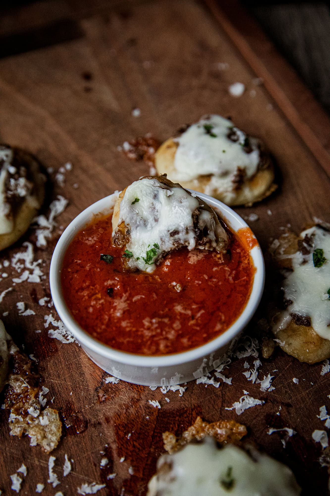 Close-up of mini meatball sub bites topped with melted cheese and herbs, served with marinara sauce.